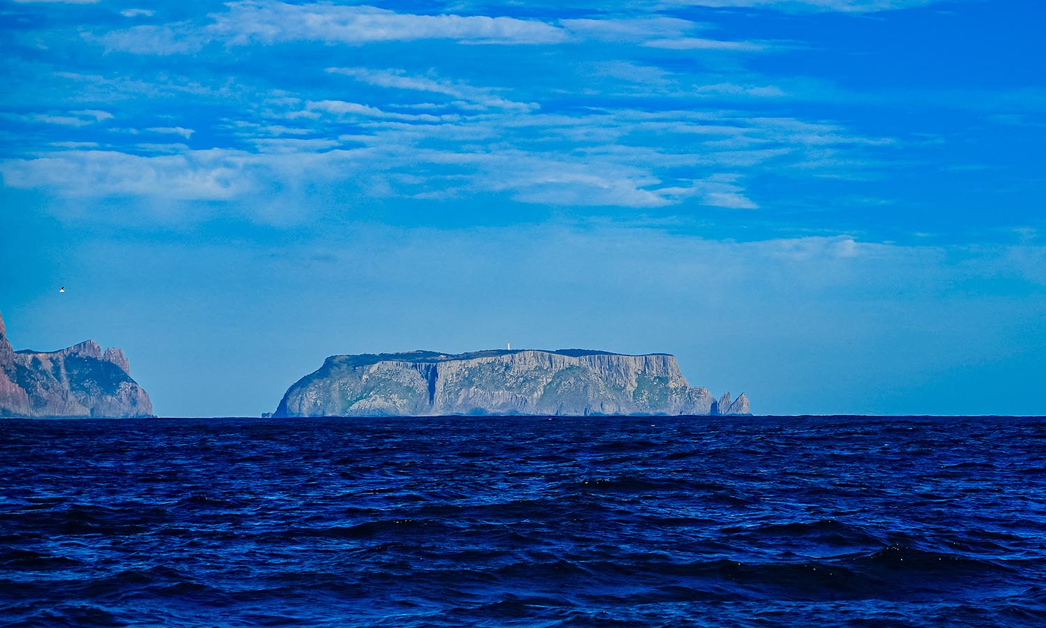 Tasman Island in the distance, surrounded by blue choppy waves.