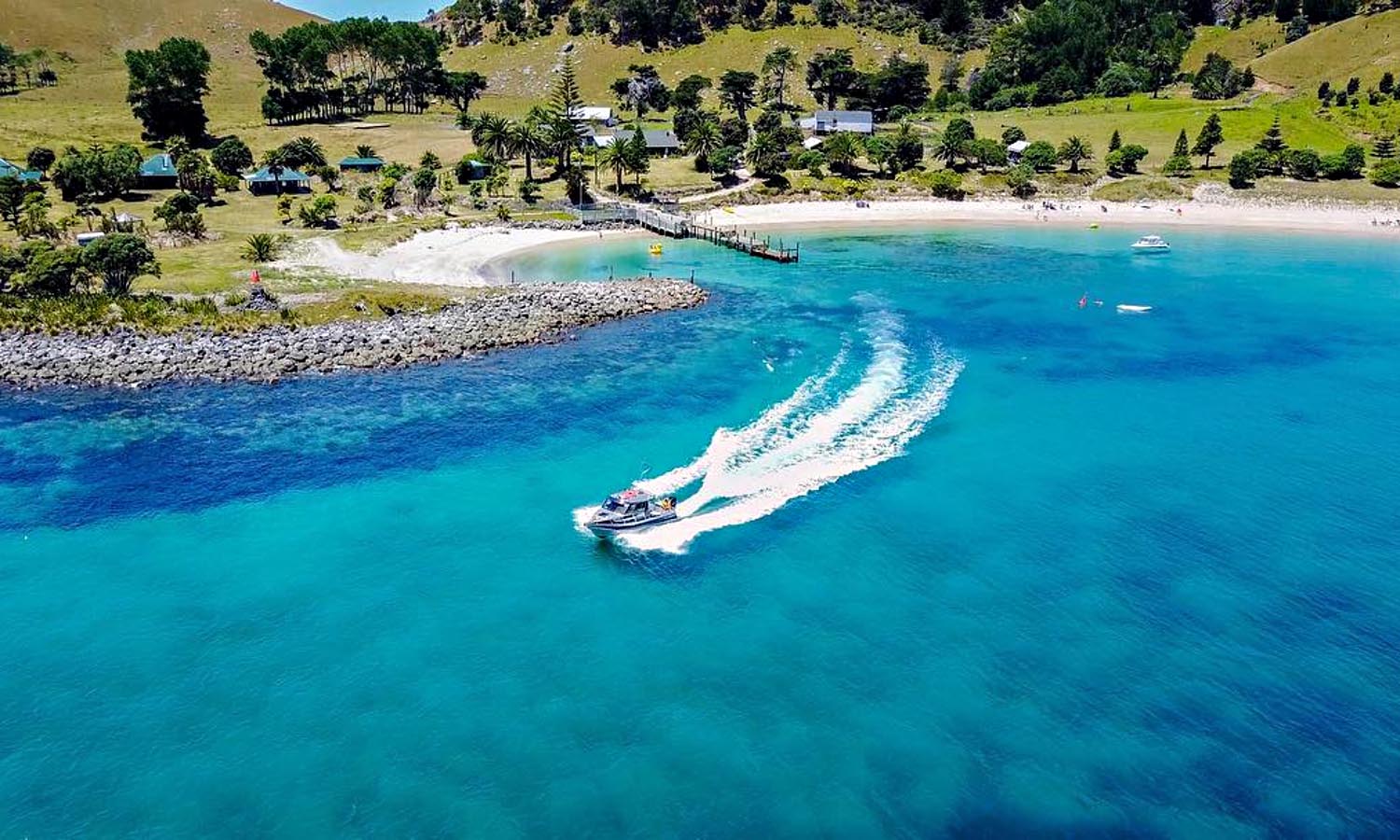 A small boat speeds away from the jetty on Slipper Island, gliding over turquoise water.