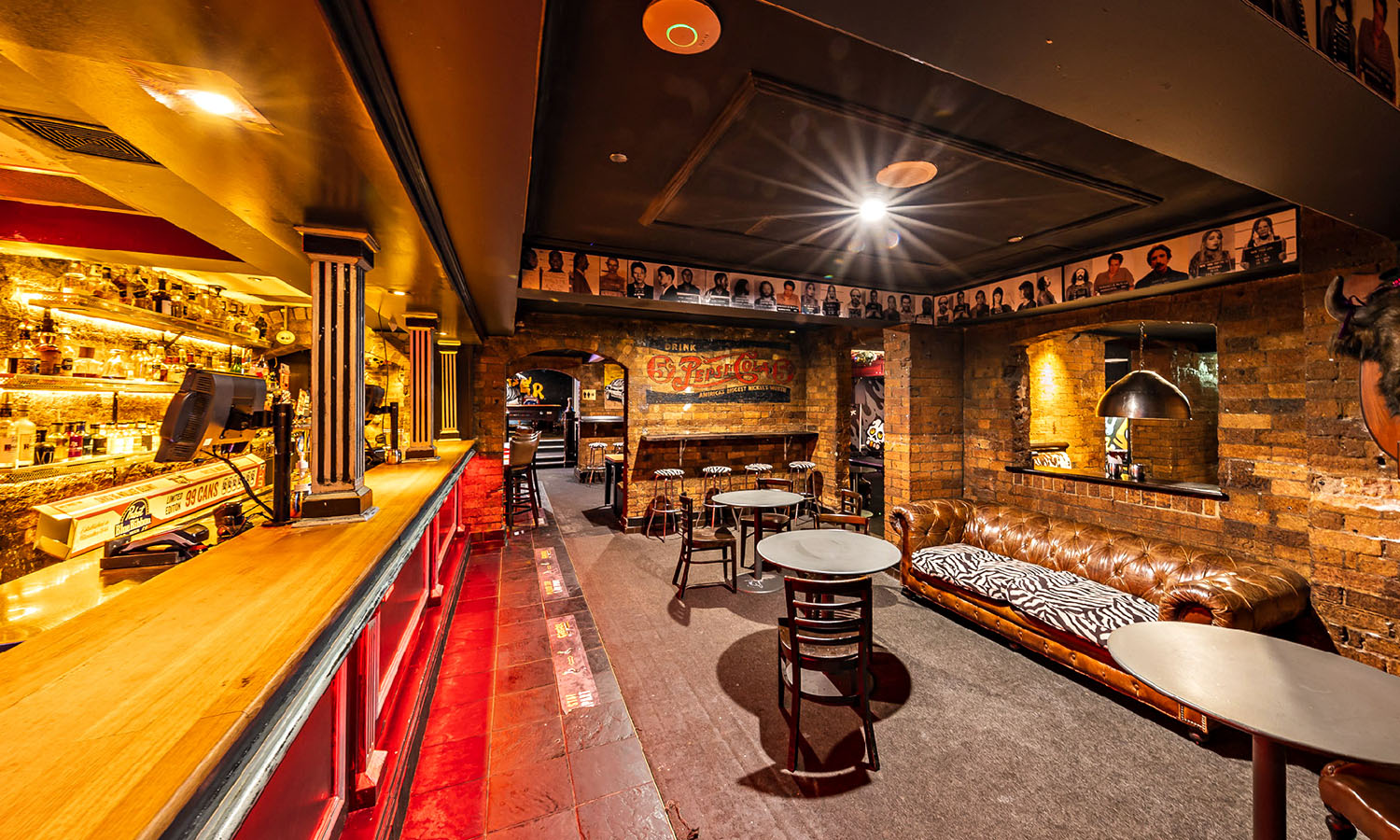 A classic bar interior with leather couches, exposed brick walls, neon lights and bar stools.