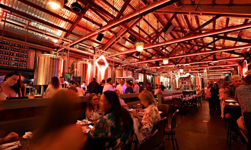 A bustling crowd enjoying drinks and food in a neon-lit room at Felons Brewing Co.