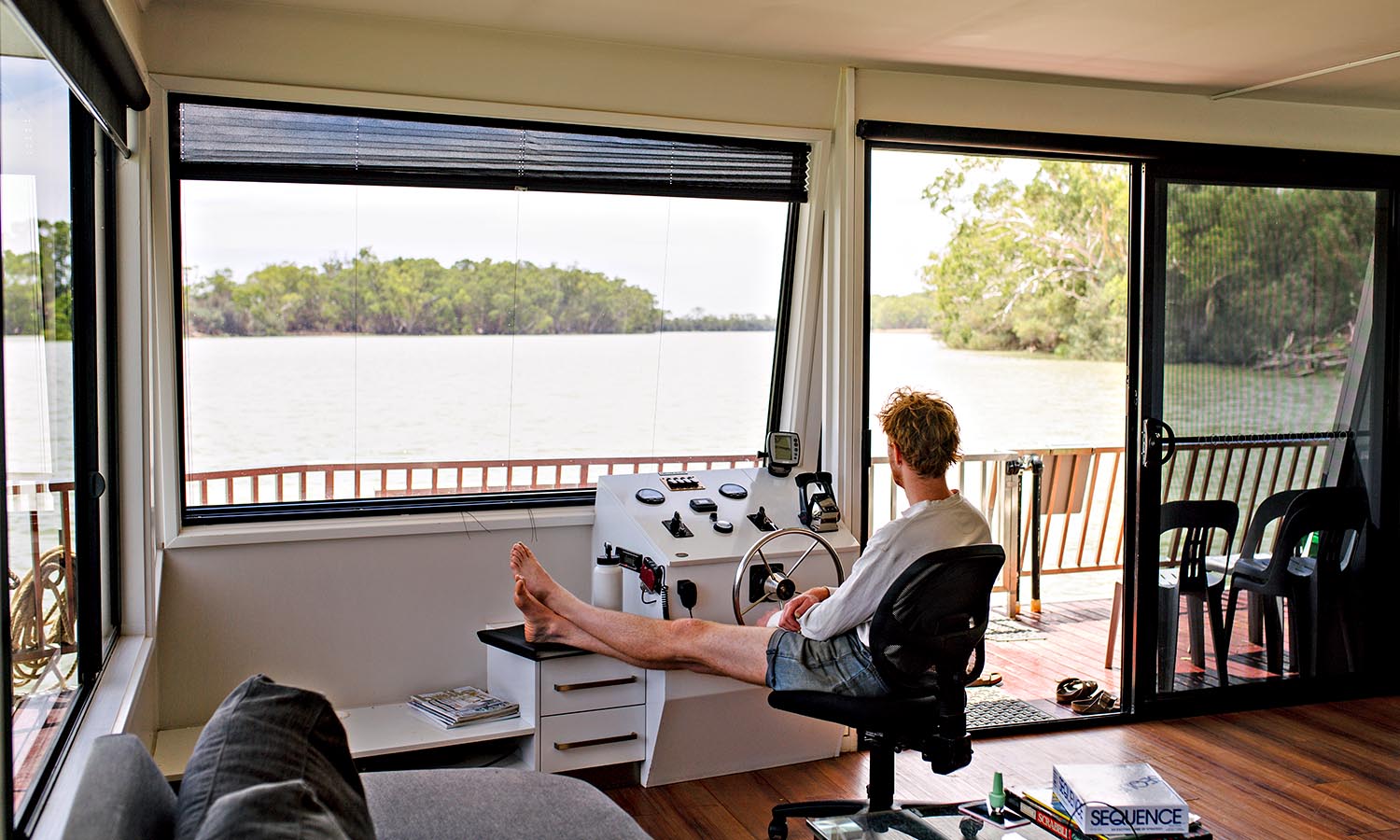 A man sits behind the wheel of a houseboat as it glides down the Murray River. 