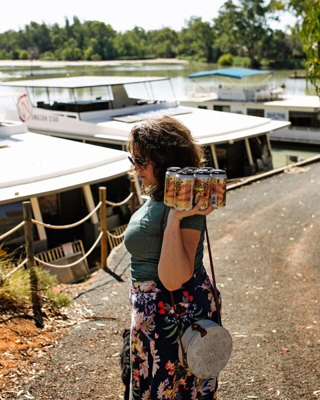 A woman holds a 6 pack of beer as she's about to board a houseboat. 