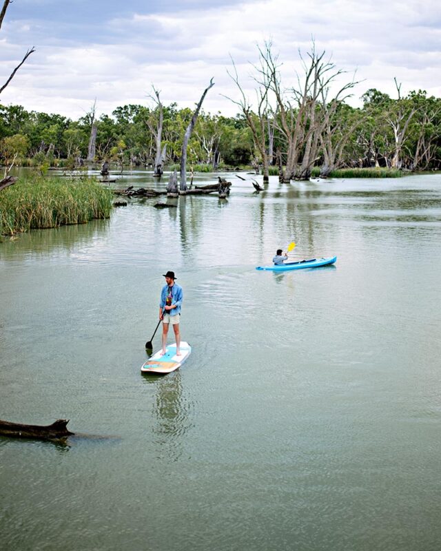 One man paddleboards on the Murray River while another, kayaks.