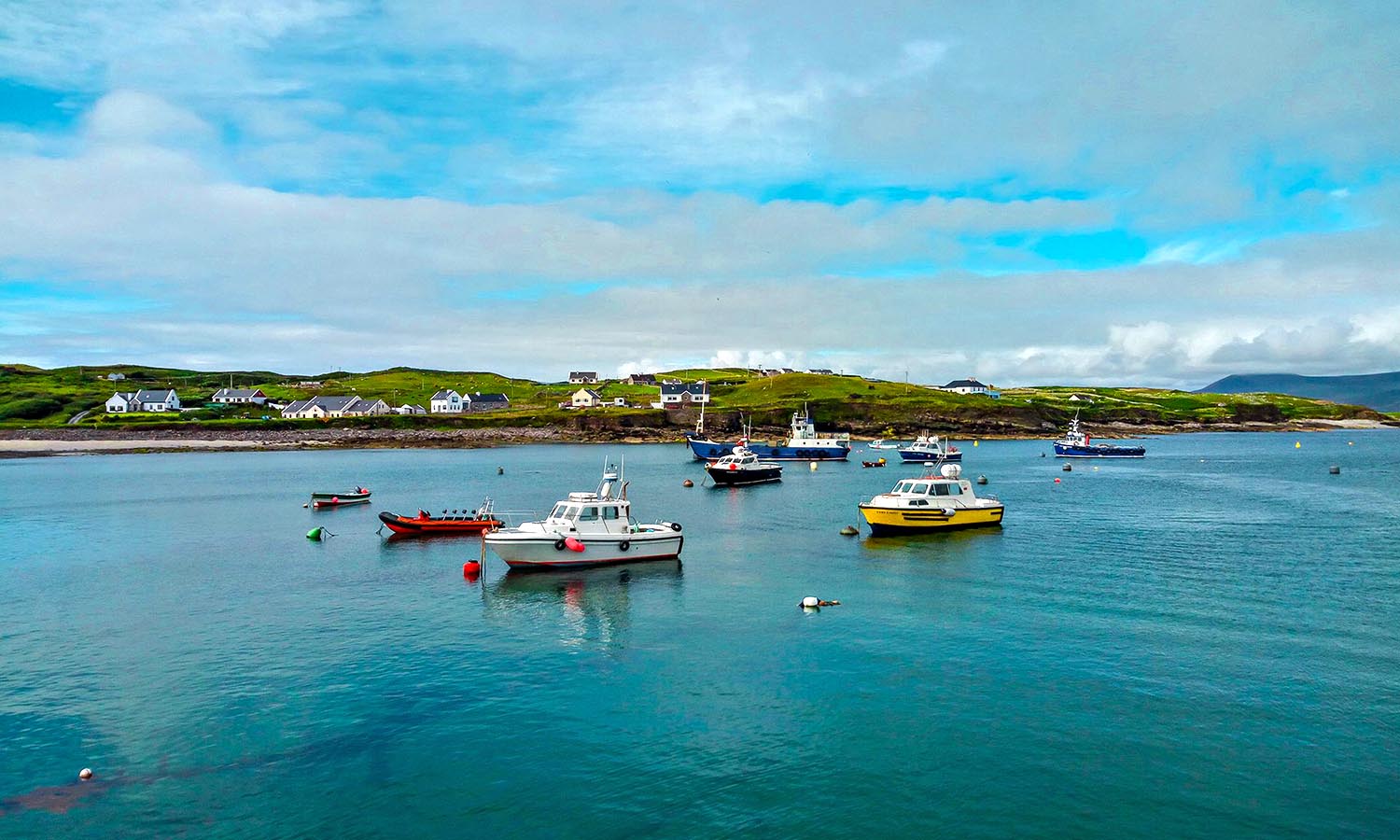 A group of boats bob on the calm water's surface of Clare Island.