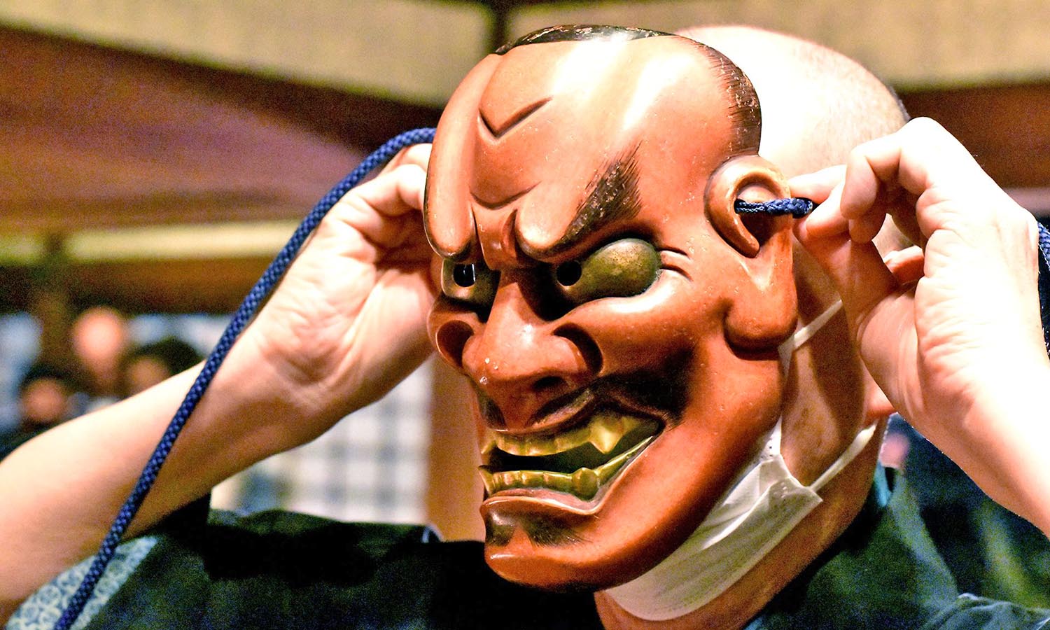 A man hides behind a traditional Japanese mask. 