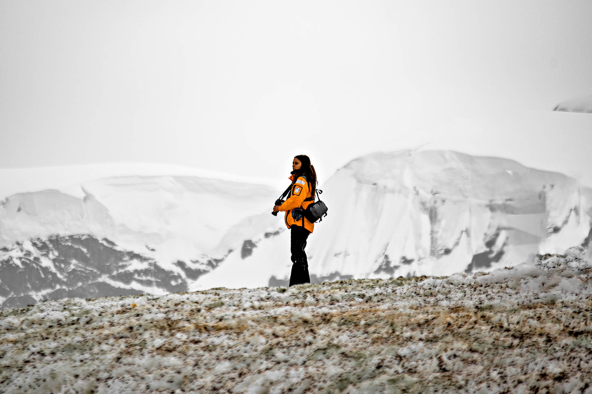 A lone woman stands on the icy ground of Antarctica.
