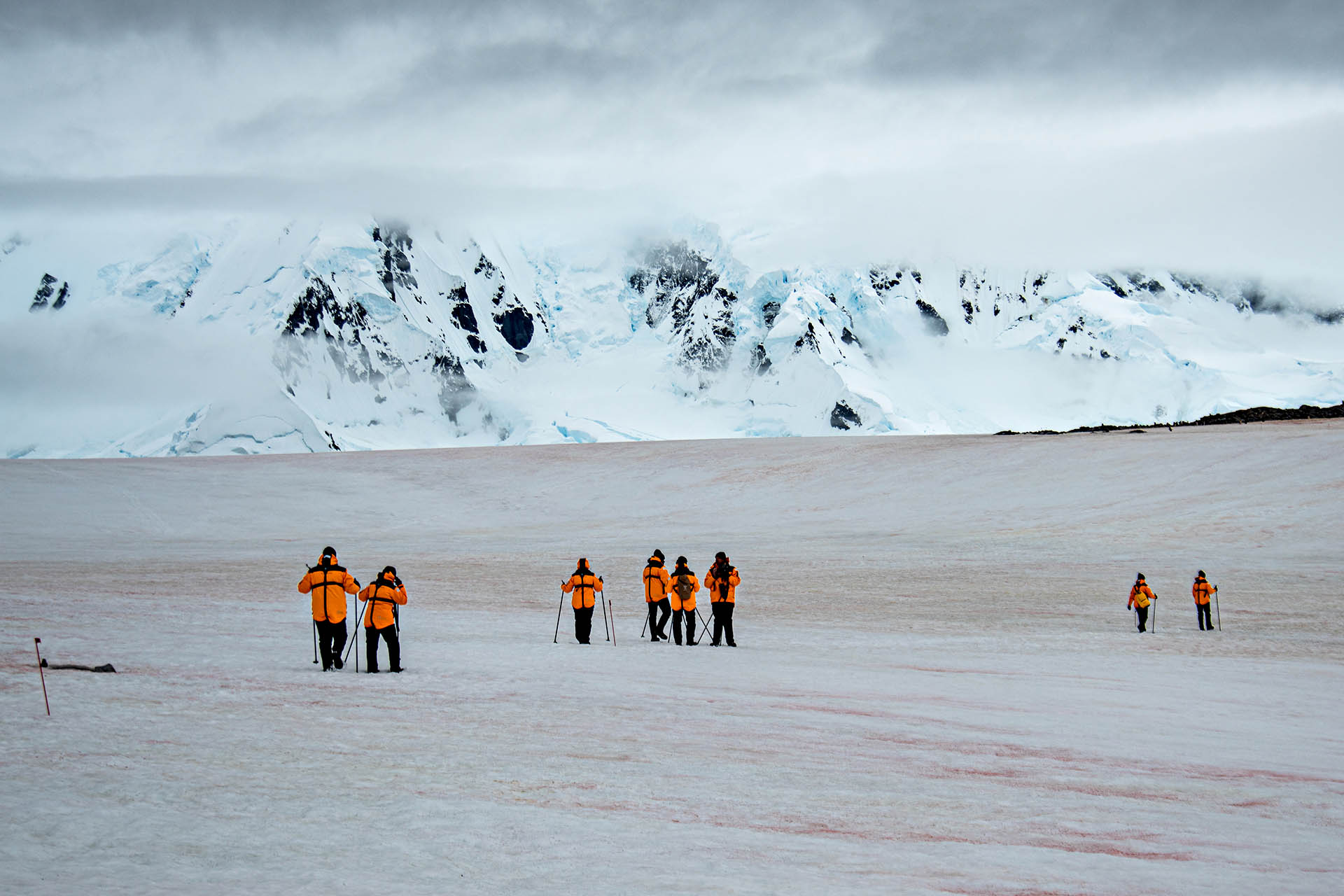 A group of people wearing brightly coloured clothing walking on the icy landscape of Antarctica.