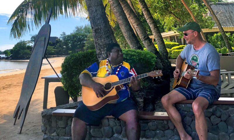 Two men playing guitar on a beach on Turtle Island in Fiji.