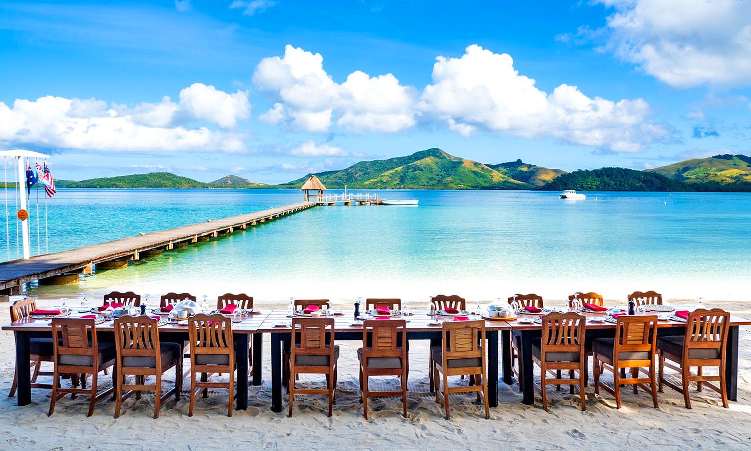 A long dining table fully set up on one of Turtle Island's white sand beaches, overlooking the water.