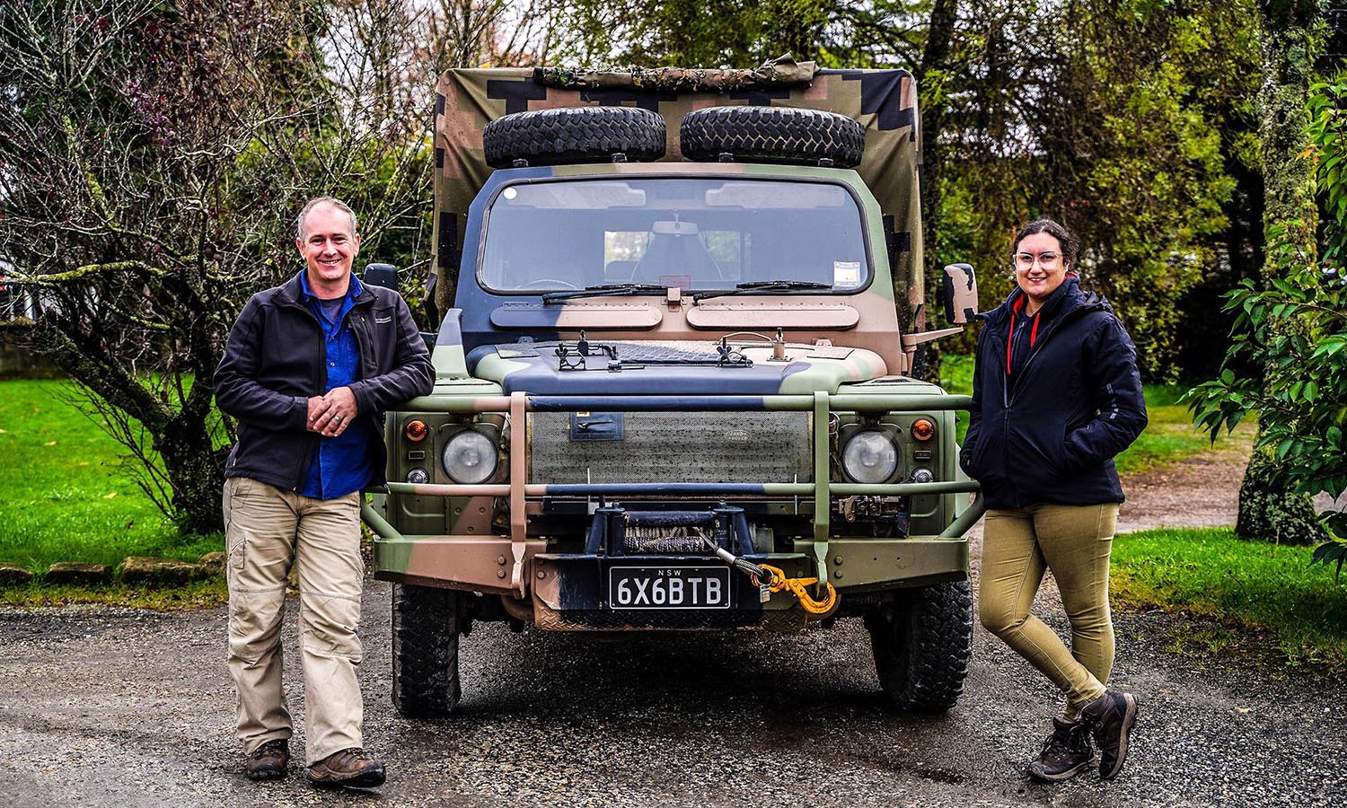 A couple standing on either side of a army coloured truck. 