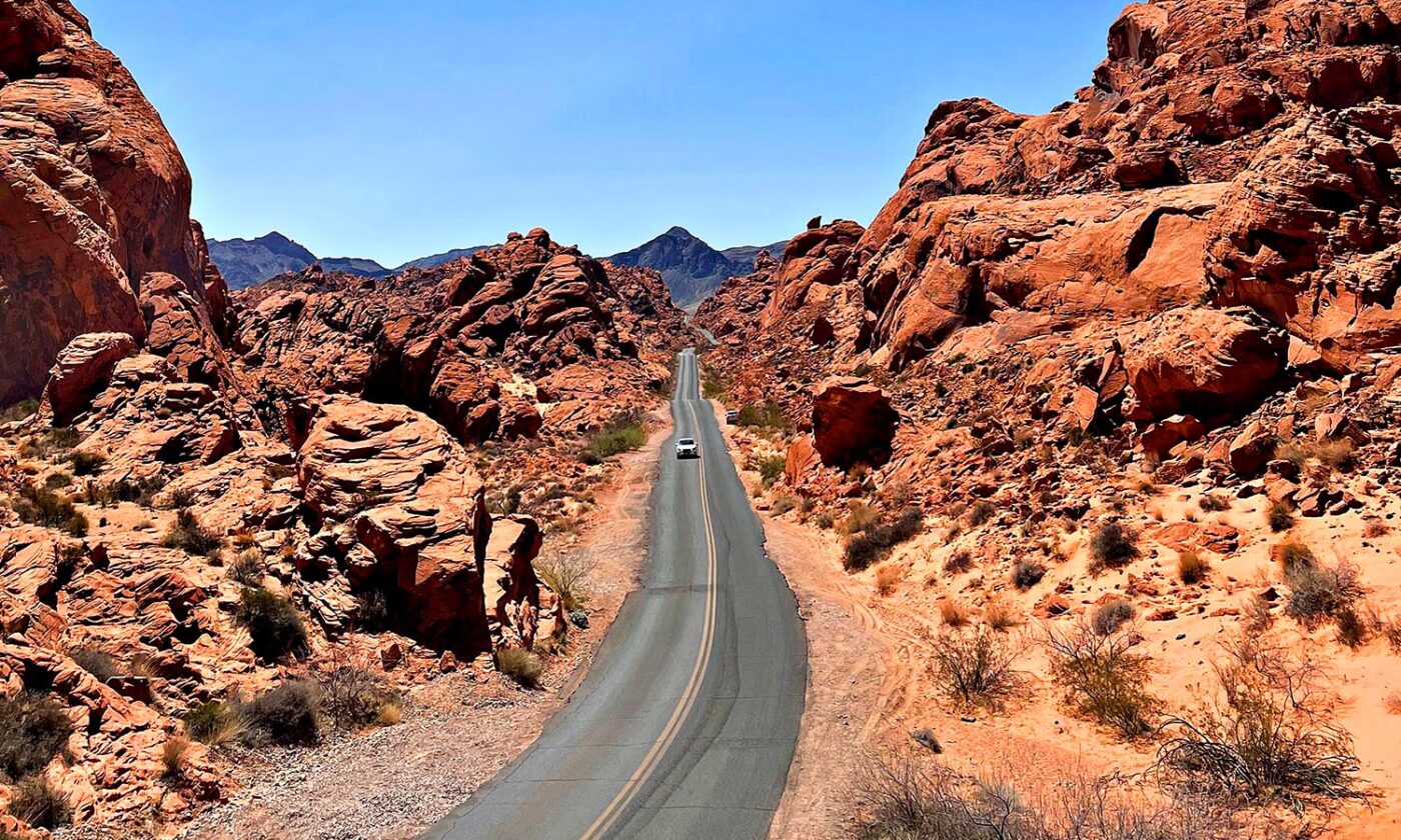 A lonely car travelling down a road in Nevada through a rocky landscape. 