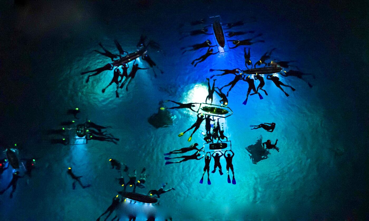 Night snorkellers gathering beneath illuminated boards during a manta ray experience on Hawaii's Kona Coast.