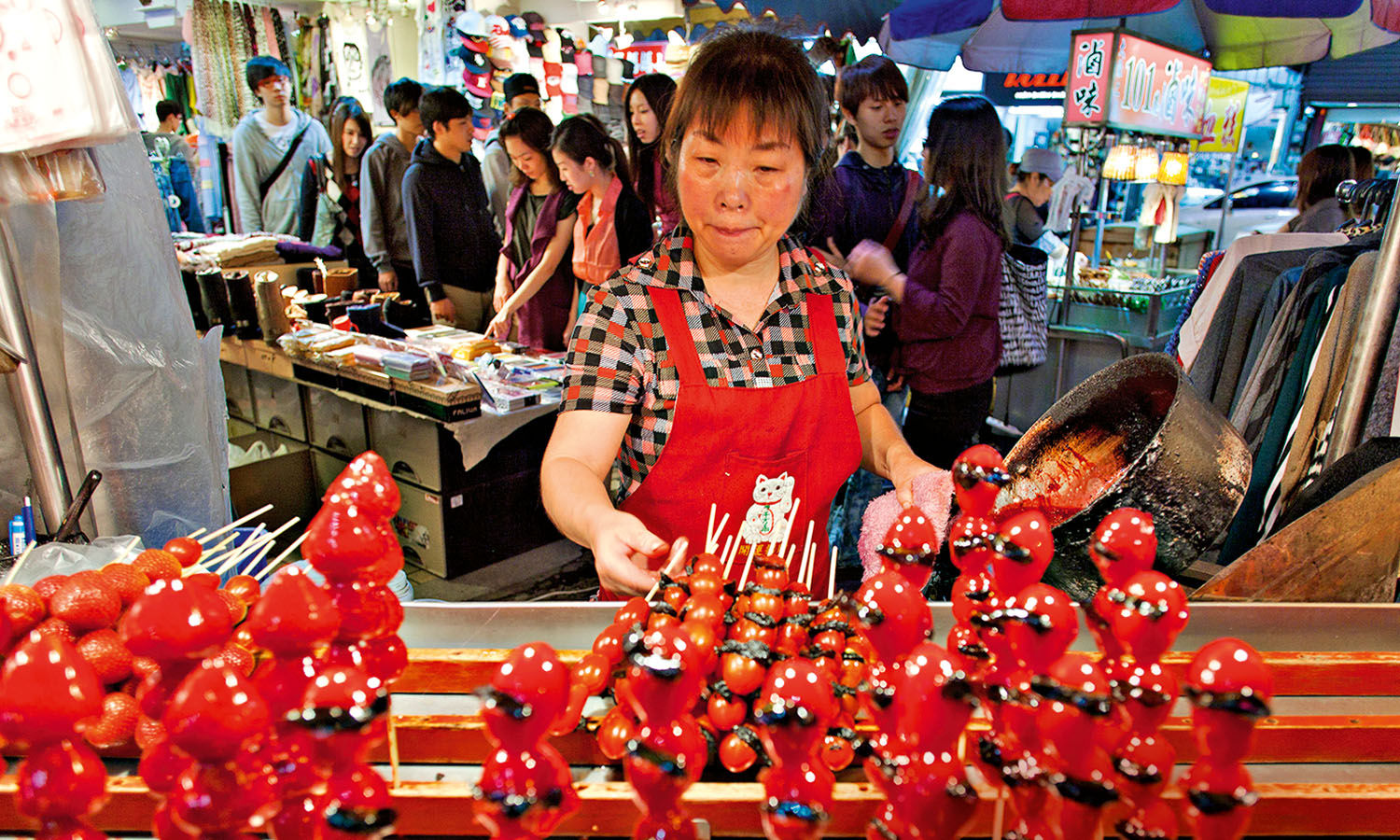 Local street food vendor turning over strawberry skewers at a food market in Taipei.
