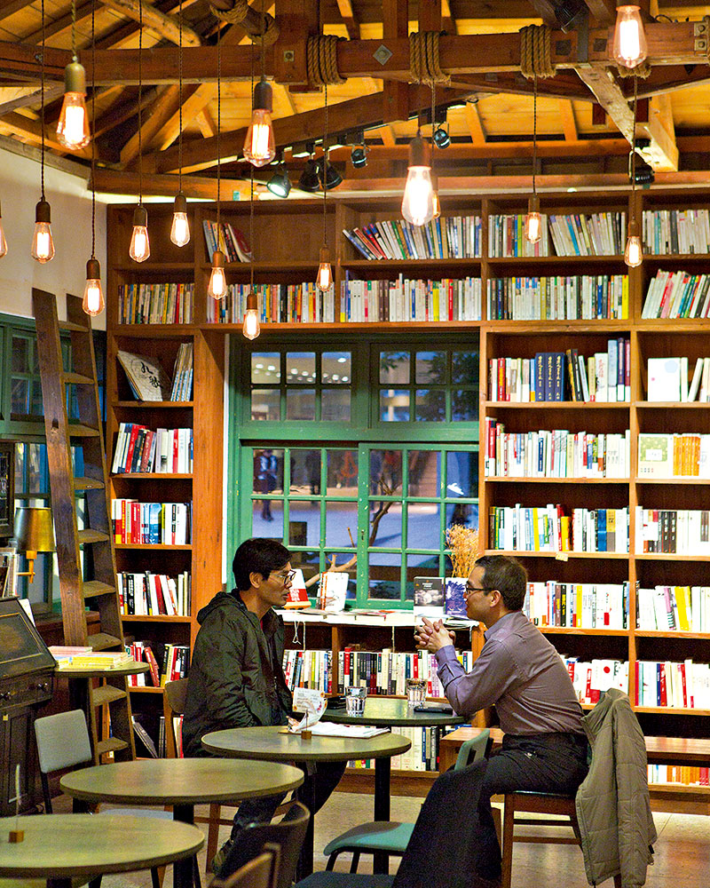 Two local men sit at a table surrounded by bookshelves in a cafe in Taipei.