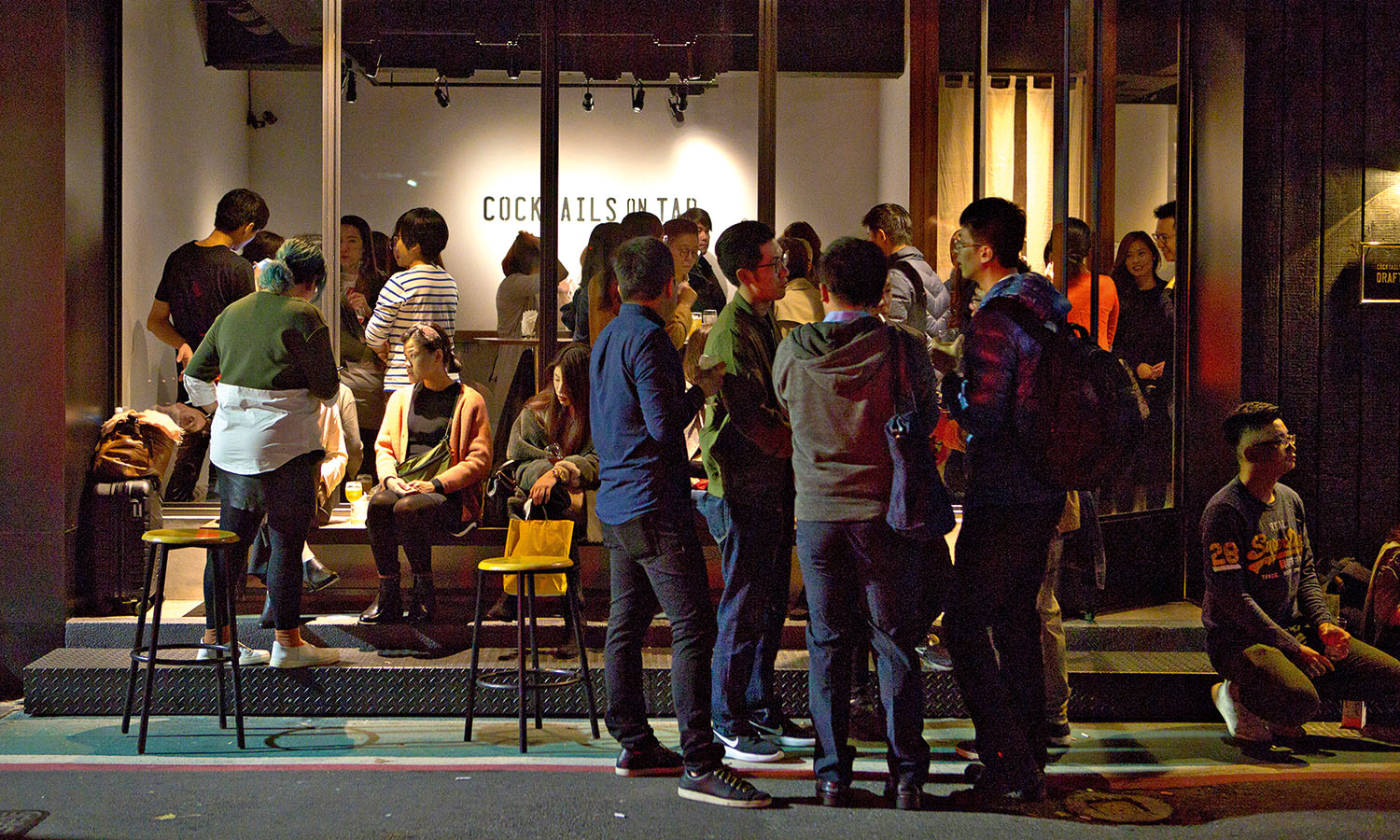 Groups of people stand outside popular cocktail bar, Da'an, in Taipei at night.