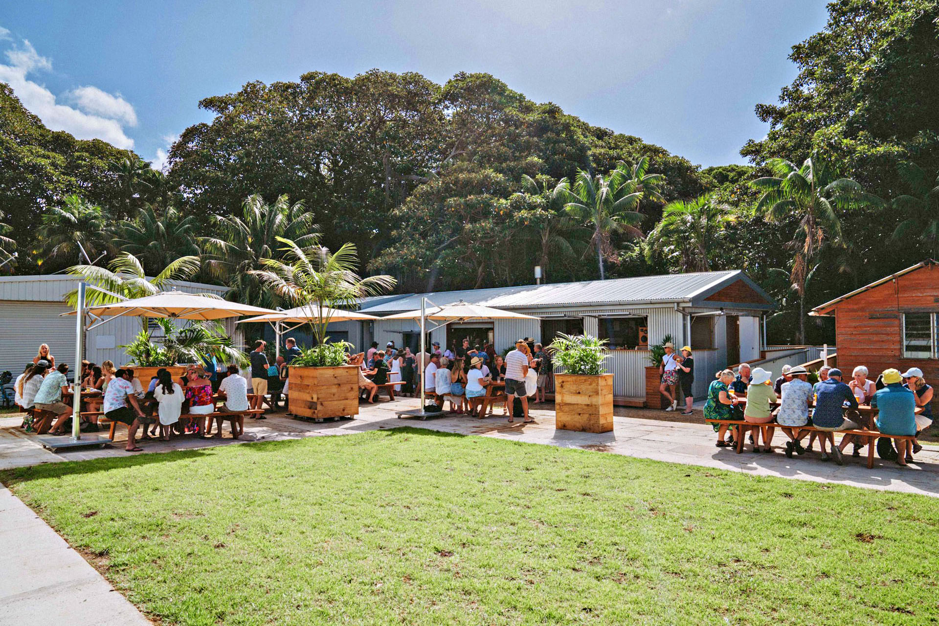 A large group of people gather in the outside section of Lord Howe Island Brewery on a clear, sunny day.