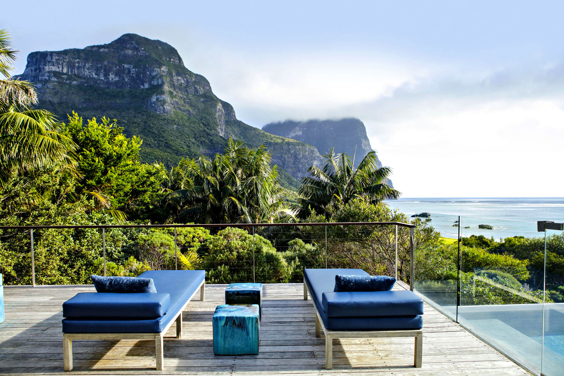 A couple of lounge chairs on a deck overlooking the luscious and mountainous Lord Howe Island.