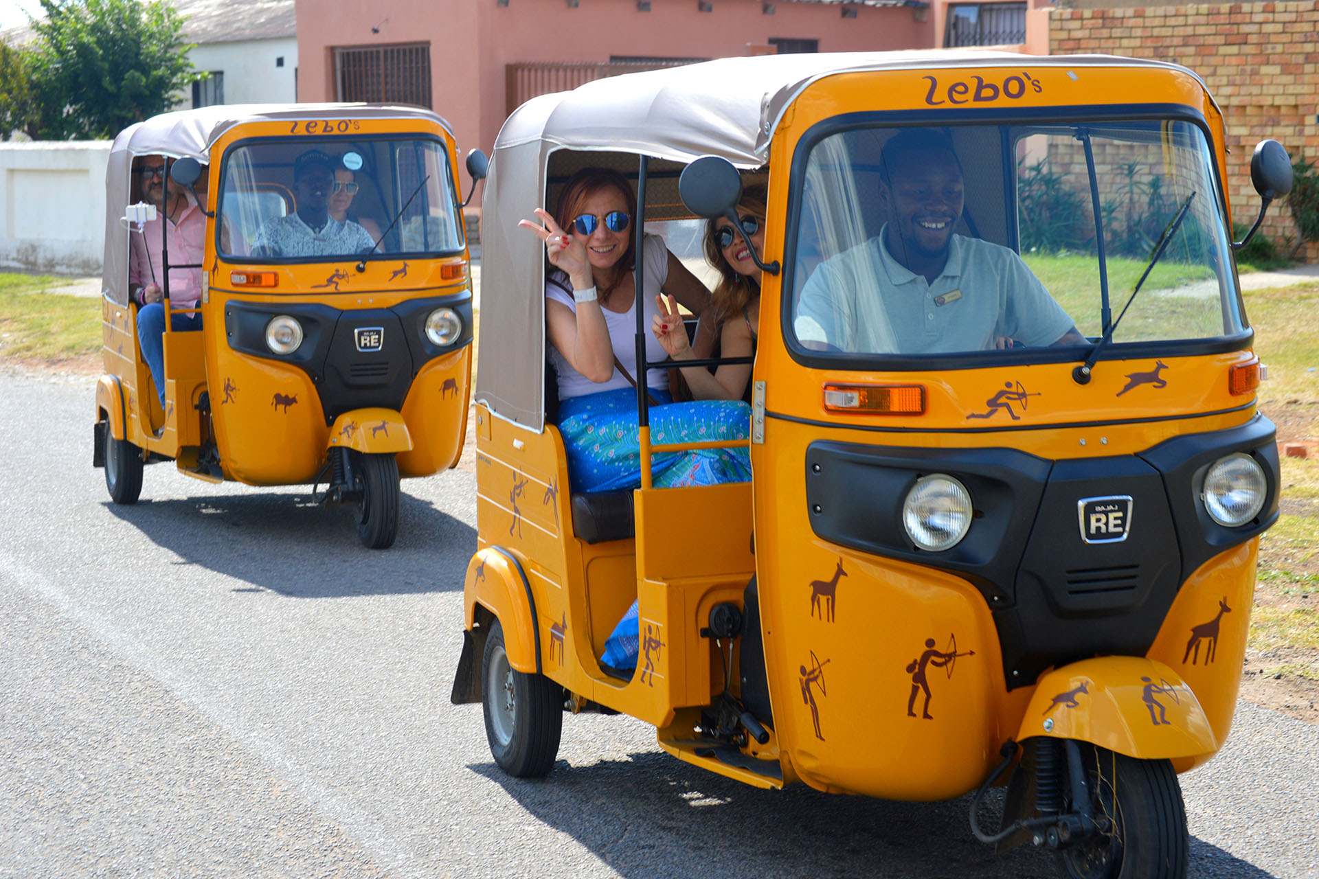 A pair of women in the back of a yellow tuk tuk in the streets of South Africa.