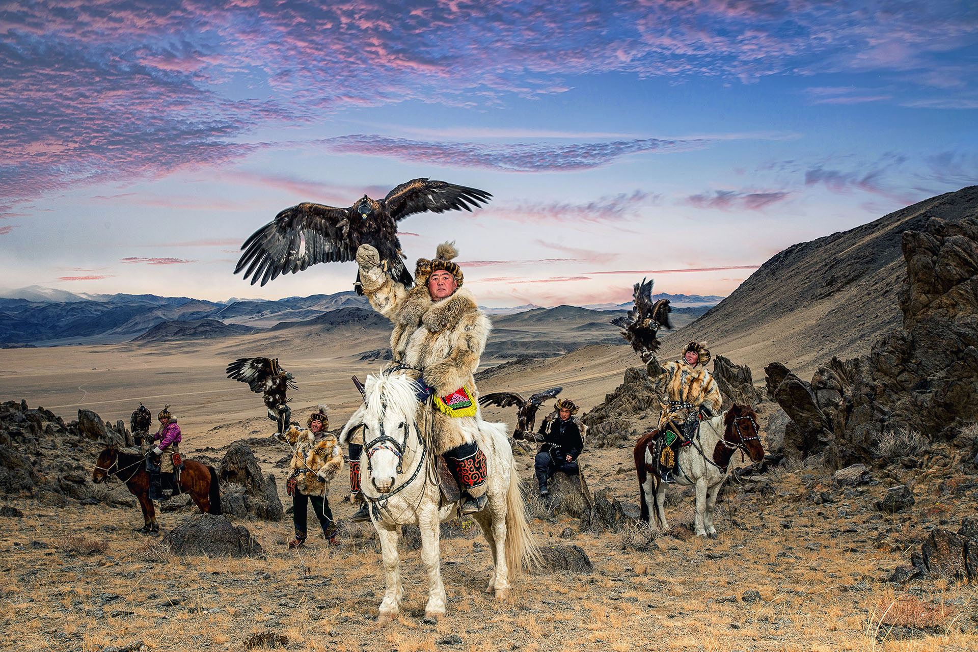 A group of Mongolian men on horseback with eagles in their palms.
