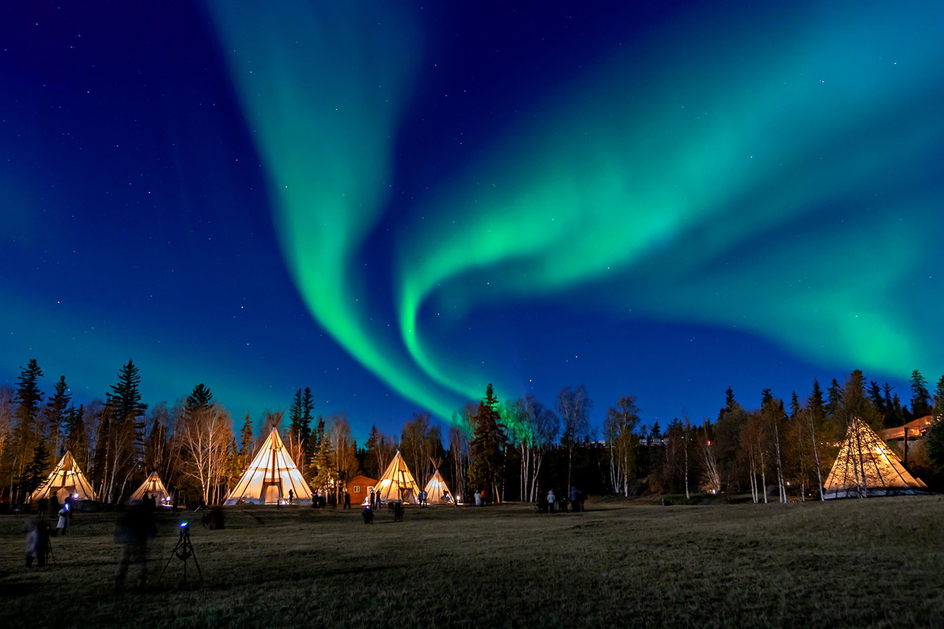 A camp of tents in Canada underneath a Northern light display.