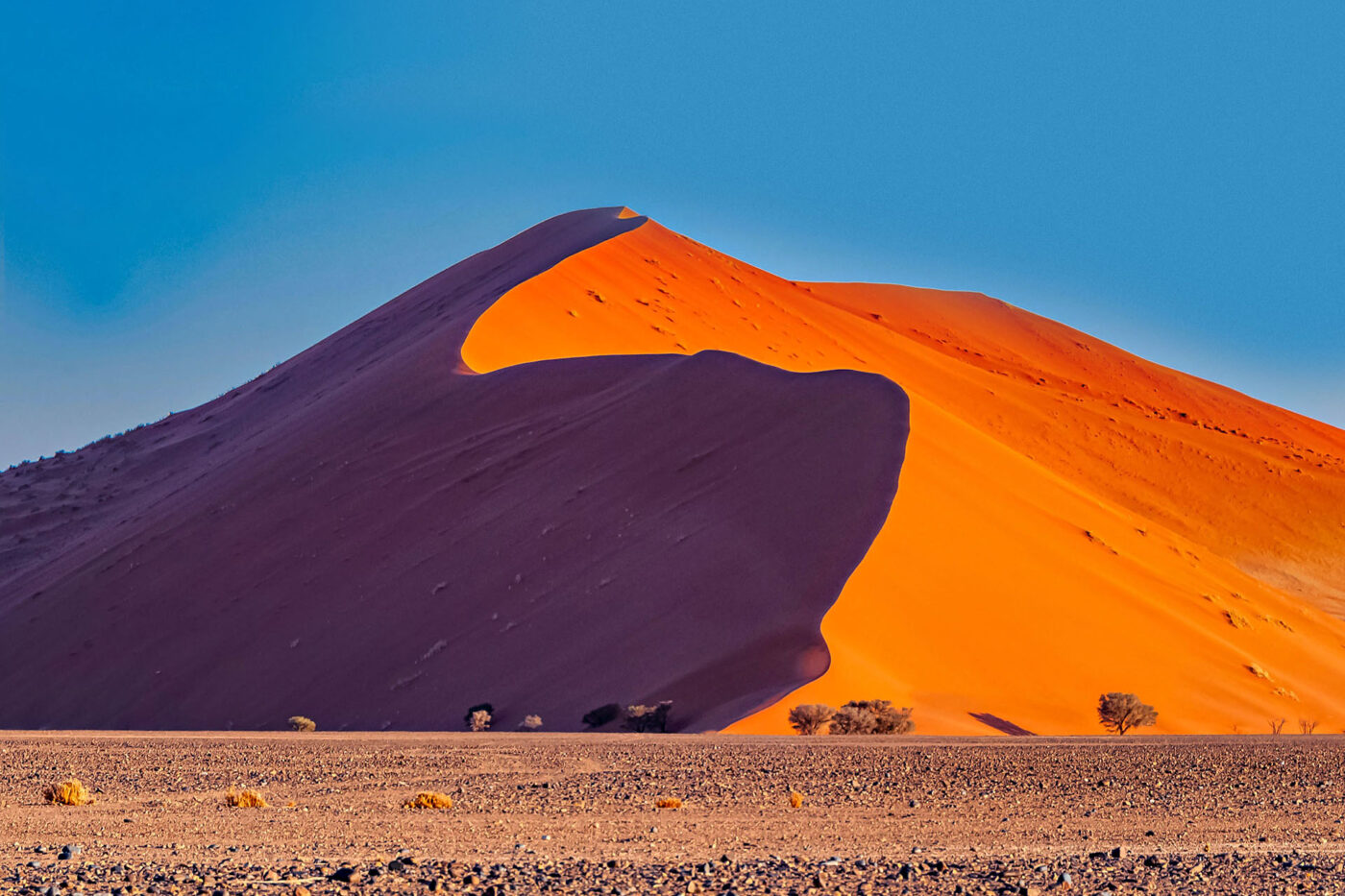 A high sandy dune reaches for the sky as the sun sets, changing its colours.