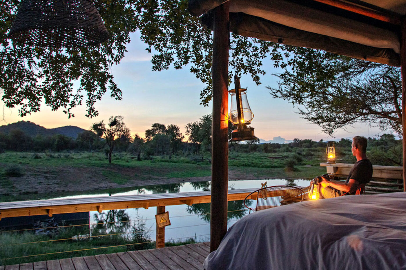 A man looks out onto a watering hole from the balcony of his lodge in South Africa.