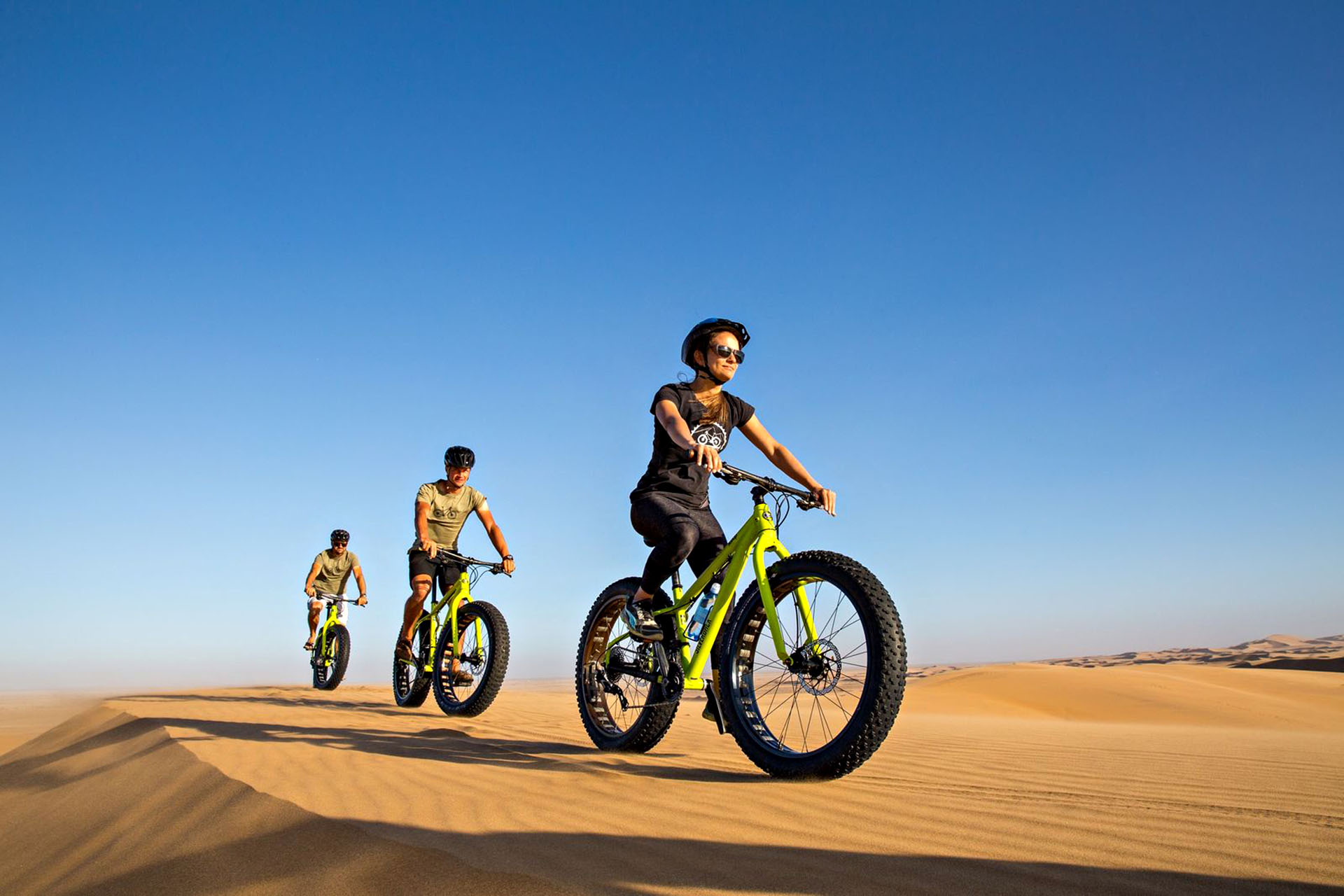 A group of people riding bikes along the sandy dunes of the Namib Desert.
