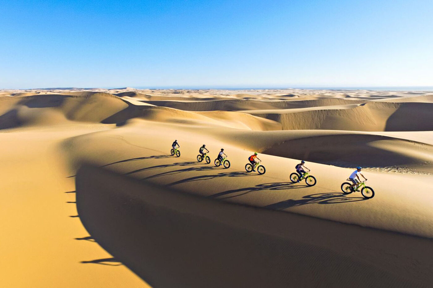 A group of people riding bikes along the sandy dunes of the Namib Desert.
