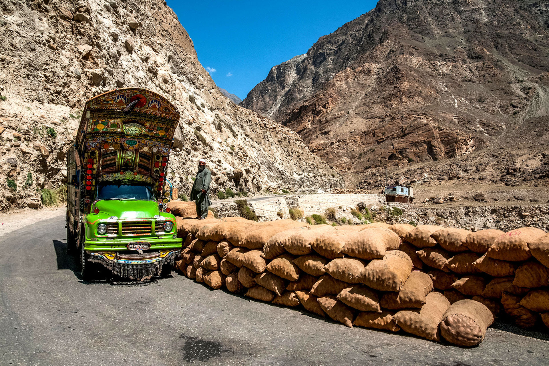 A brightly coloured bus sits next to a row of sandbags in the mountains of Pakistan.