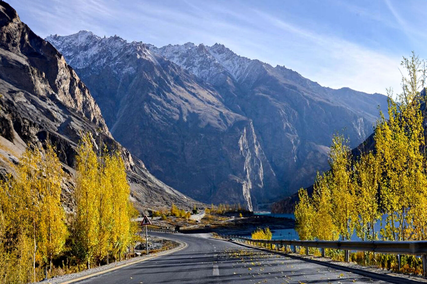 A winding highway snakes between lush greenery and snow capped mountains.