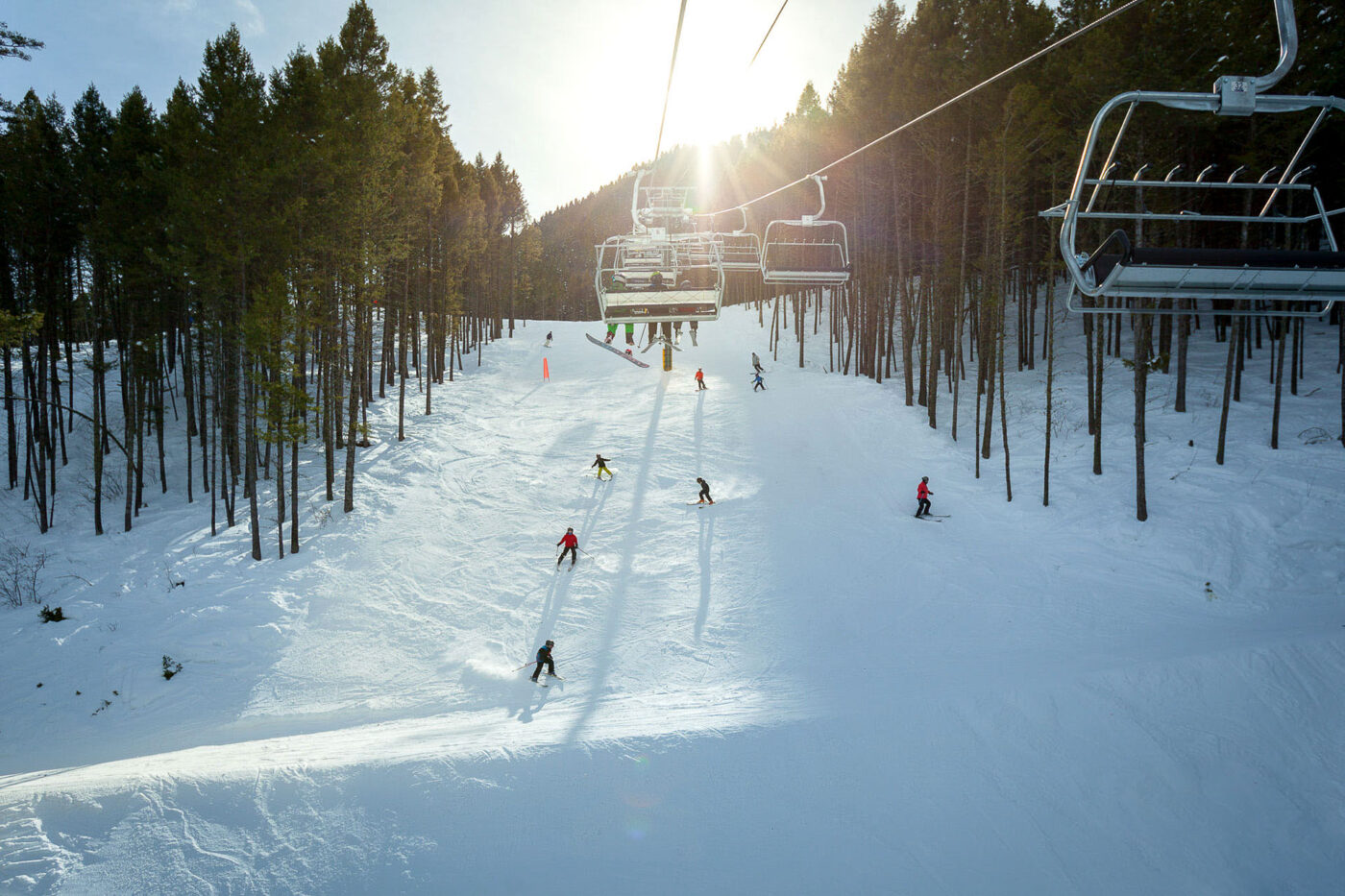 Skiers are making their way down a slope with empty chairlifts above.