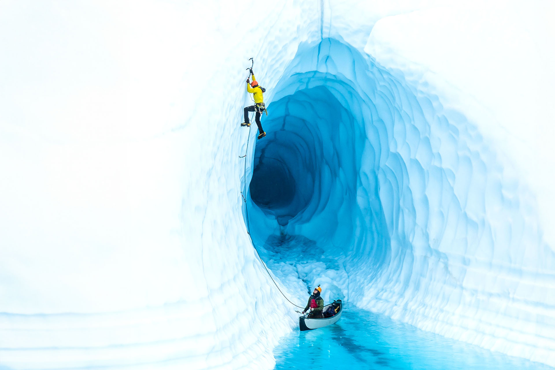 A lone man using icepicks to climb up the side of a glacier in Alaska.