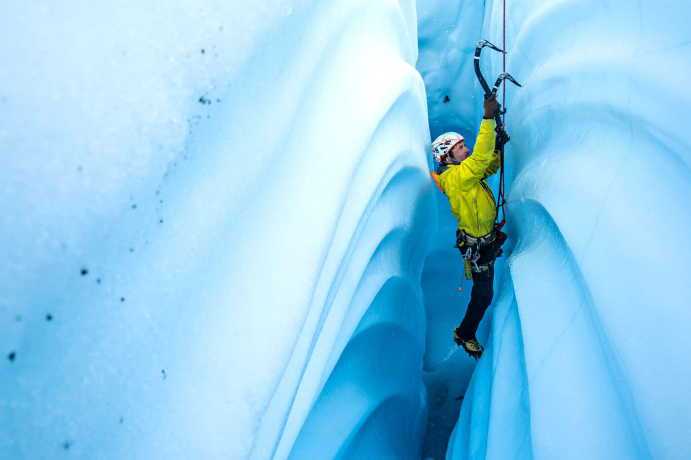 A man uses ice picks to climb up the side of a glacier in Alaska.