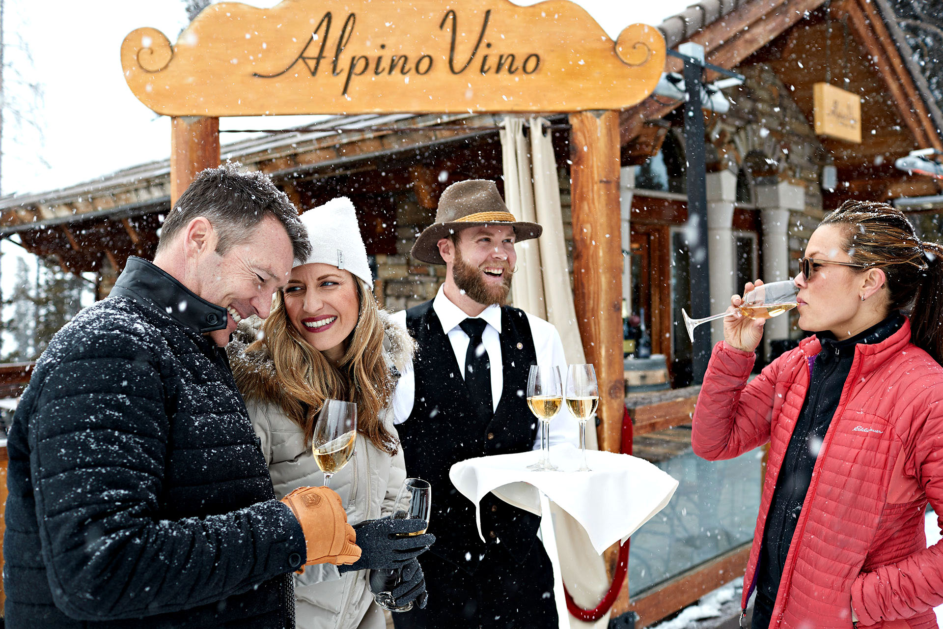 A group of people enjoying a glass of Alpino Vio wine as snow falls outside a lodge in Telluride.
