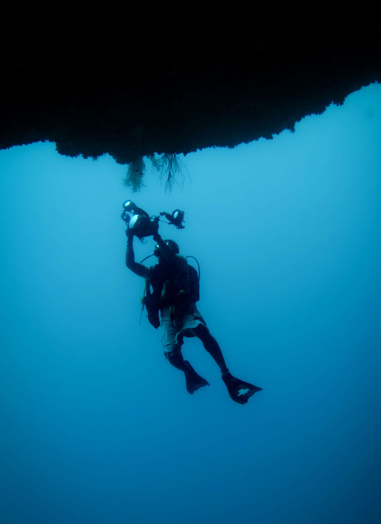 A lone diver swims towards a coral shelf with an underwater camera.
