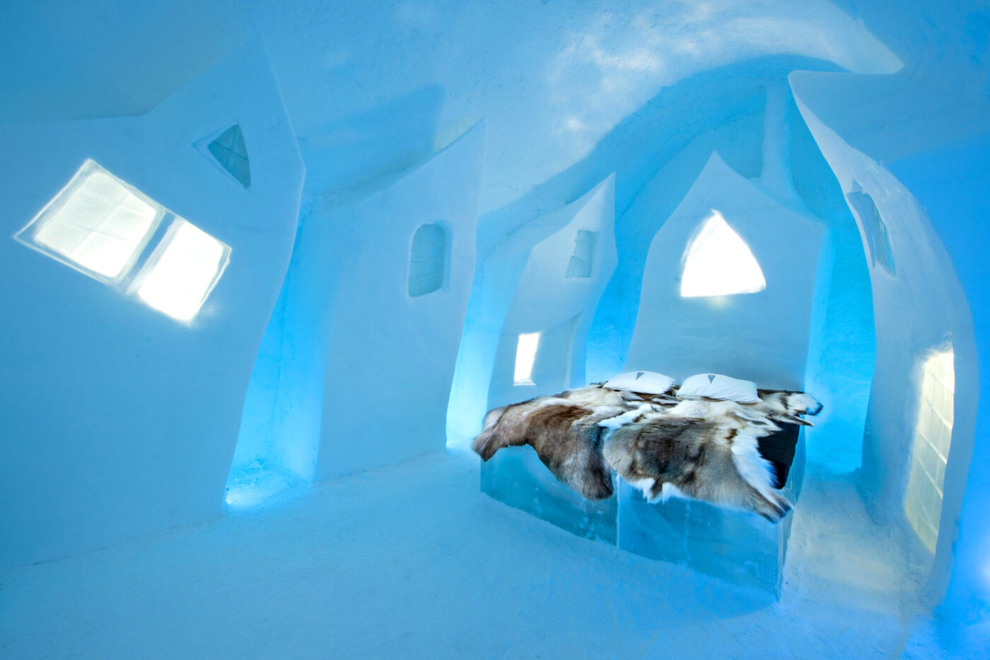 A bed, made completely out of ice, sits in a room, also made out of ice.