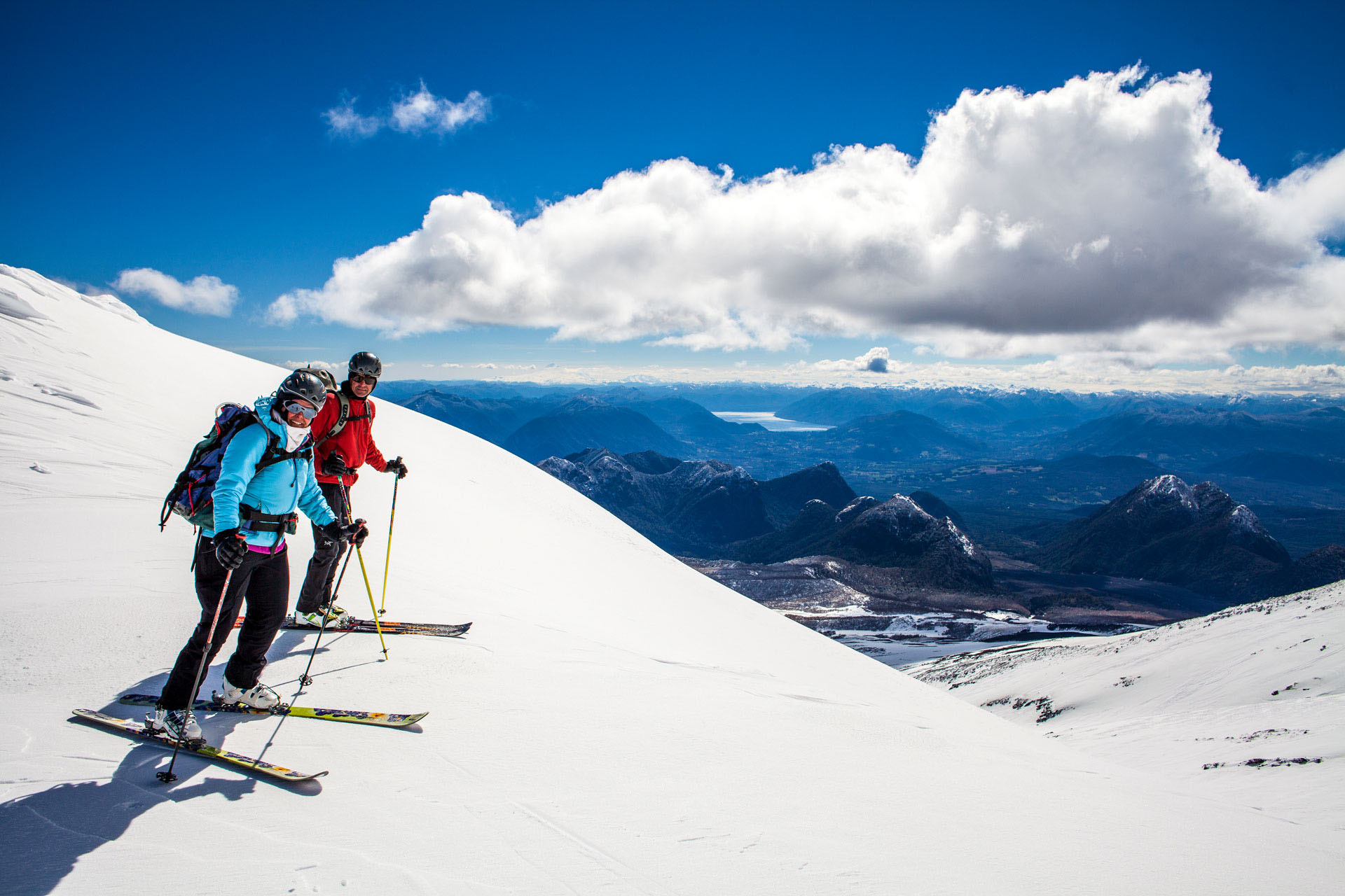 A couple going skiing down an snow-covered volcano in Chile.
