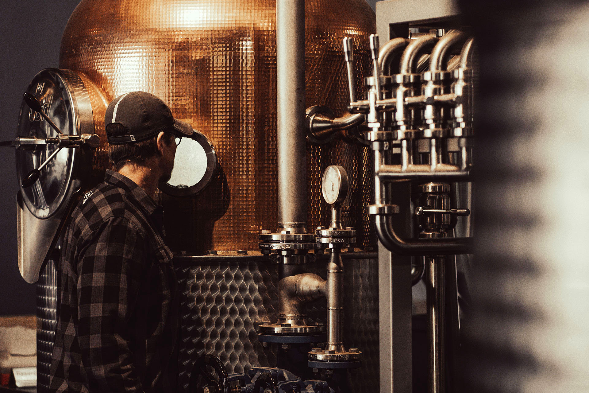 A man stands in front of brewing machinery.