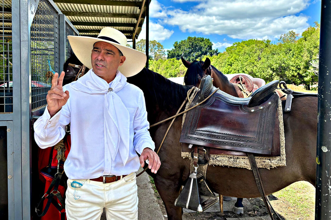 A man dressed in traditional Peruvian clothing stands in front of two brown horses on The Historic River Mill property. 