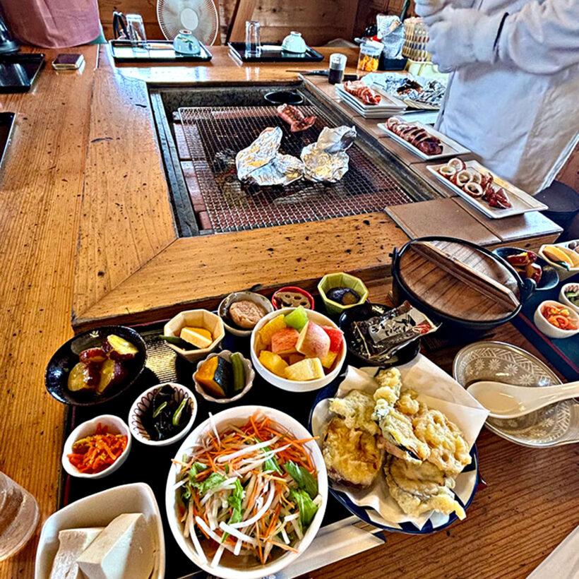 An Ama diver cooking freesh seafood over charcoal with a plate of traditional Japanese food in the foreground.
