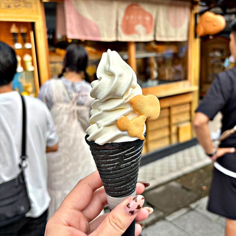 A soft serve ice cream cone with a small snoopy biscuit on the side.