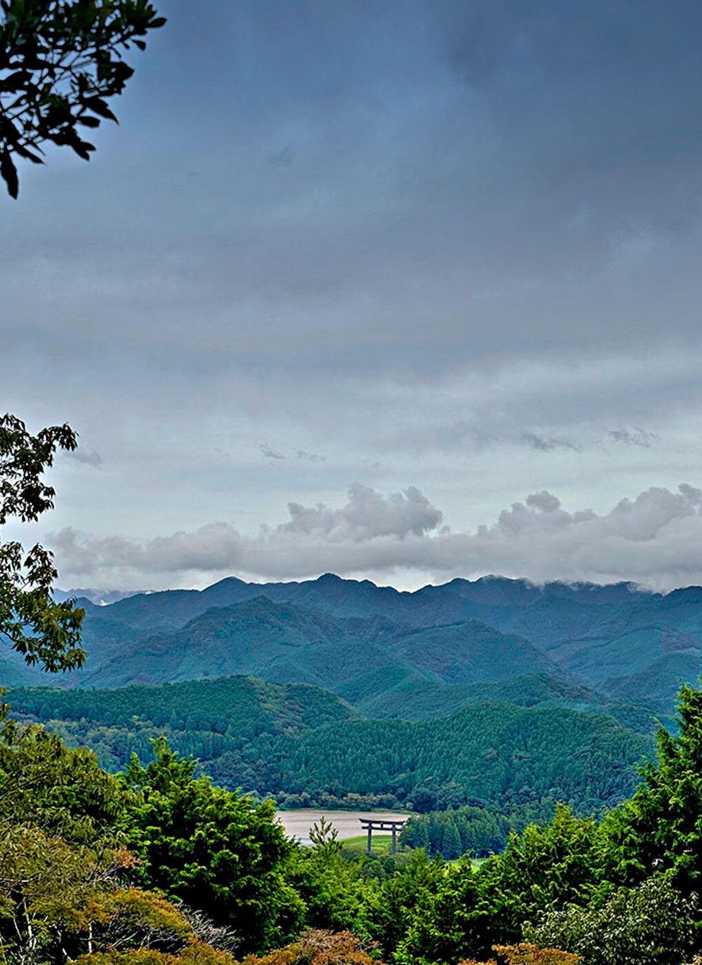 A tori bridge in the distance, with luscious greenery surrounding it.