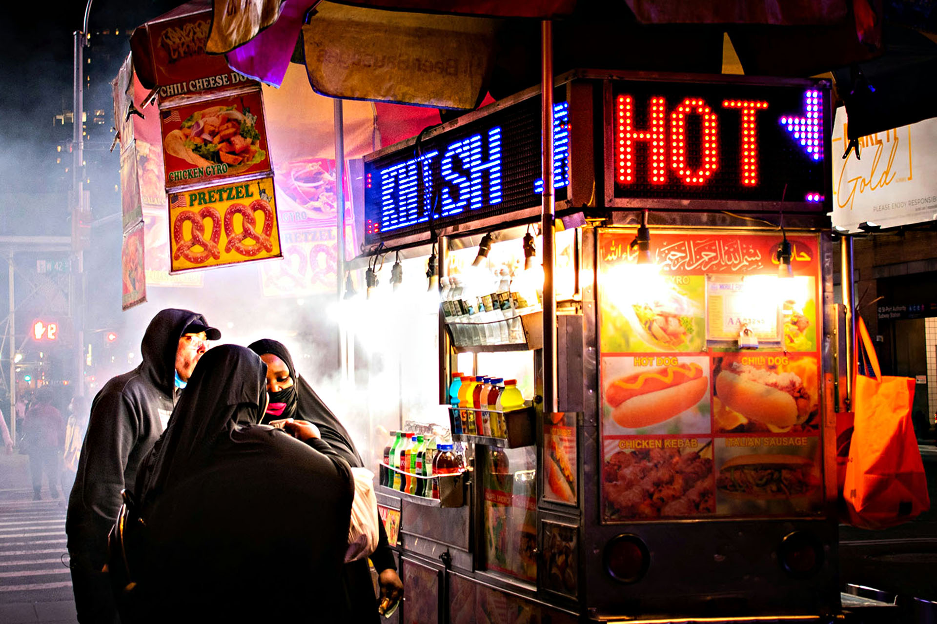 People congregate around a hot dog stand in NYC.