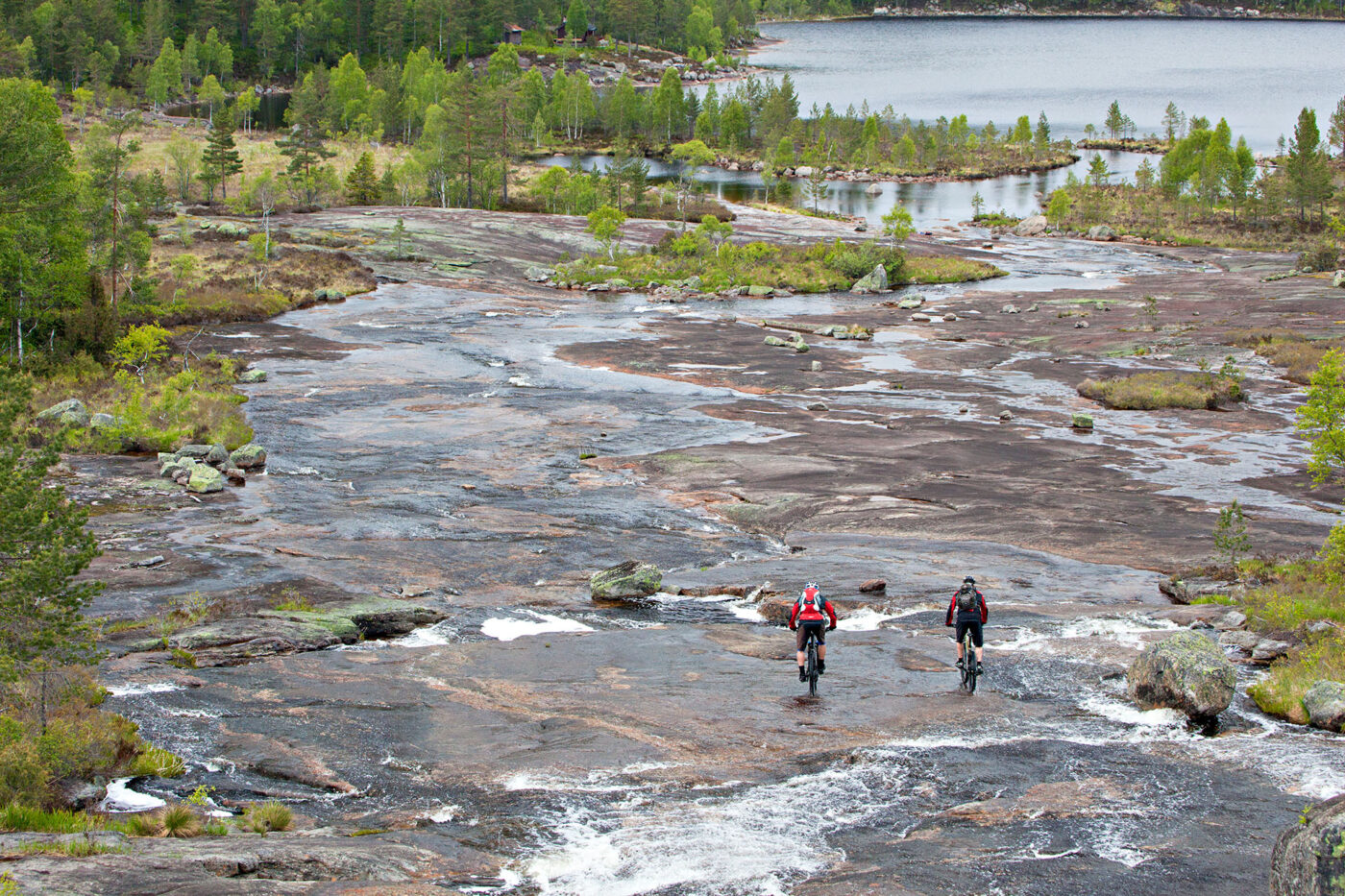 Cyclists navigate ancient granite slabs and flowing waterways on Telemark's rugged trails, showcasing the wild terrain that surrounds this off-grid glamping escape.
