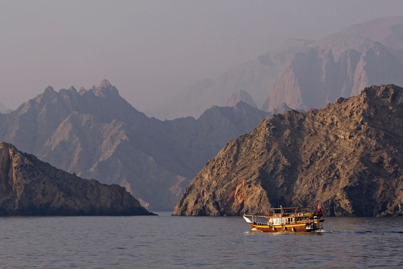 A boat motors through the waters from Sheesa Bay to Red Island, among rocky mountains.