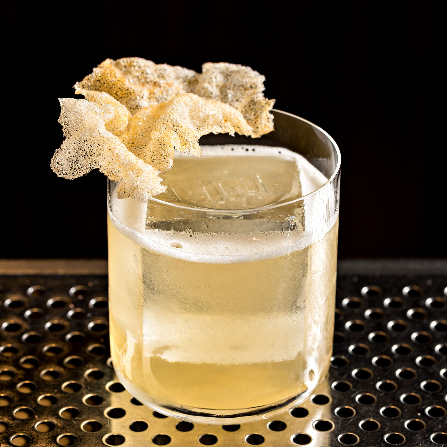 Clear cocktail topped with a crisp edible garnish served over a large block of ice.
