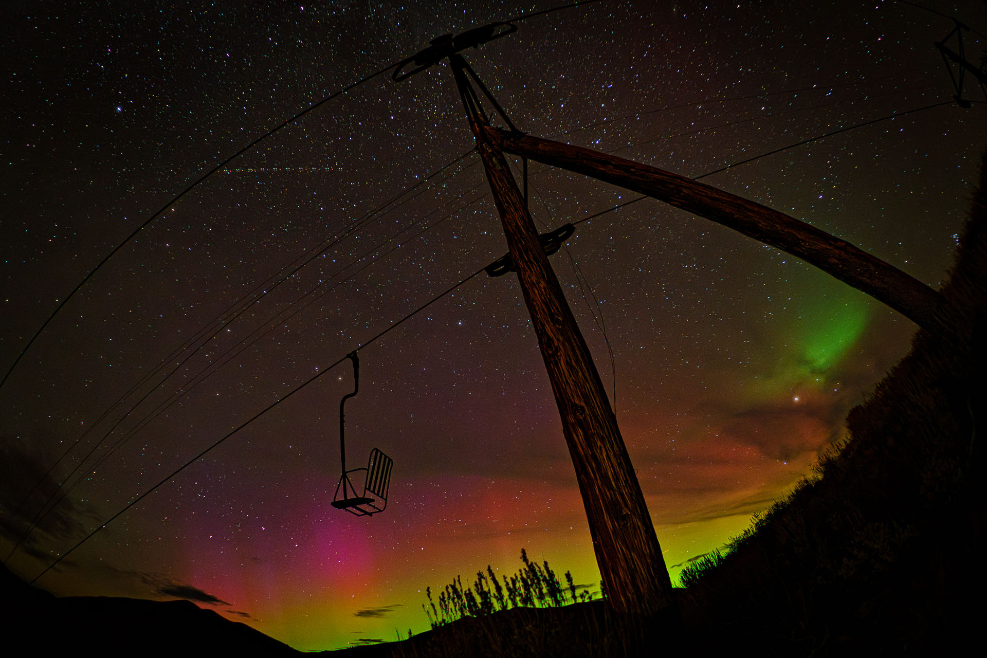 Northern Lights glow above an old ski lift and star-filled sky in Sun Valley, Idaho, USA.