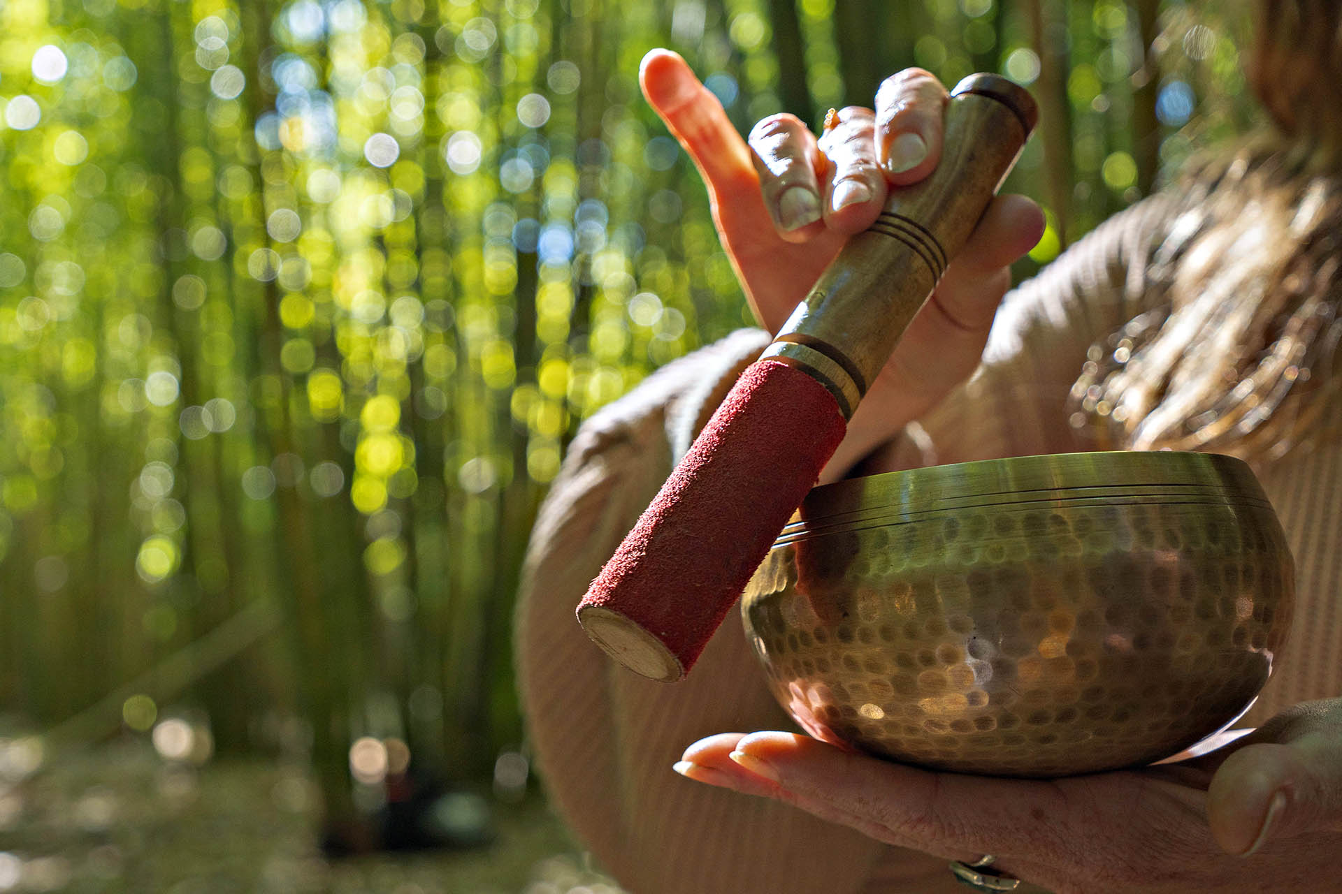 Hand striking a Tibetan singing bowl during a meditation sound recording in Kyoto bamboo forest.