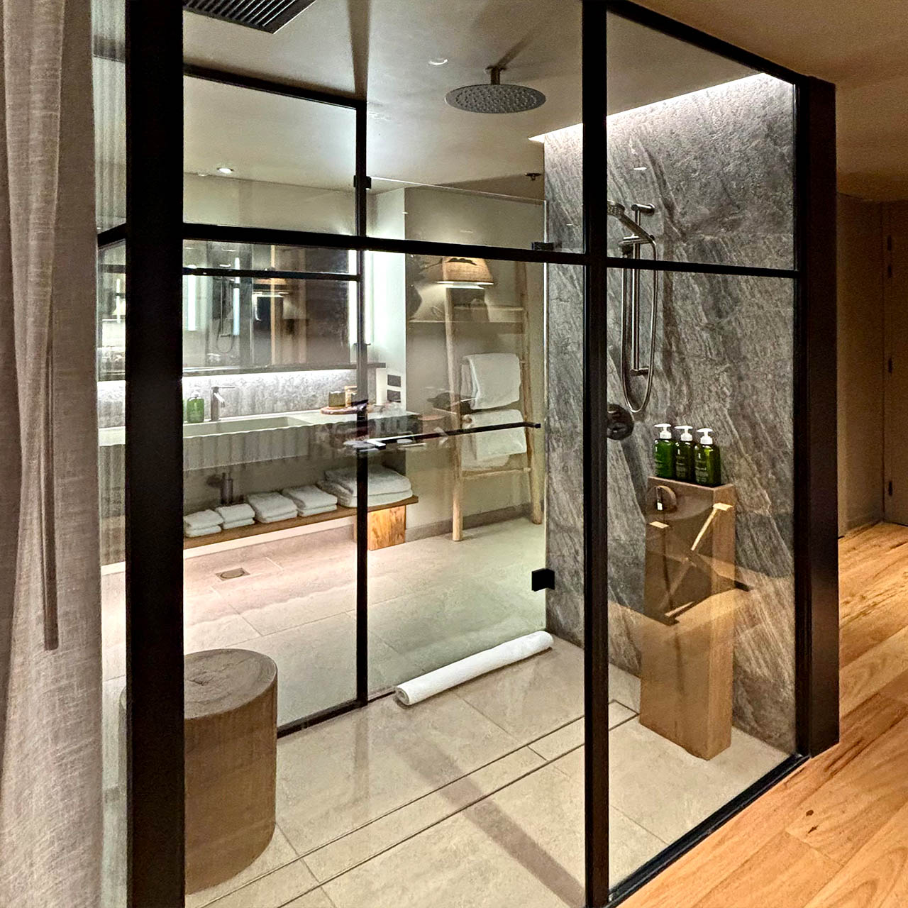 Modern bathroom at 1 Hotel Melbourne with walk-in rain shower, natural stone finishes and timber accents.