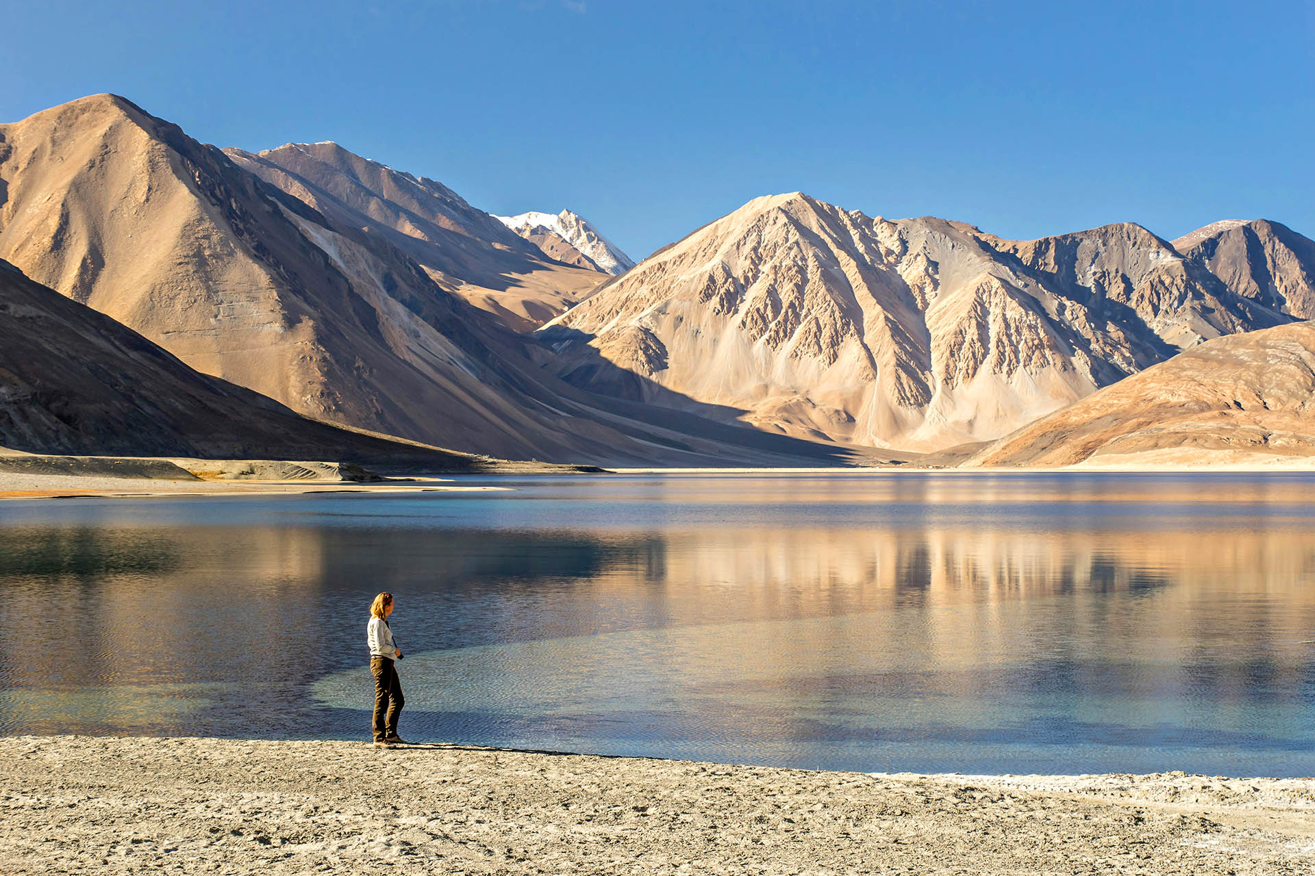 Traveller standing beside a mountain lake surrounded by the Himalayas in Ladakh, India.
